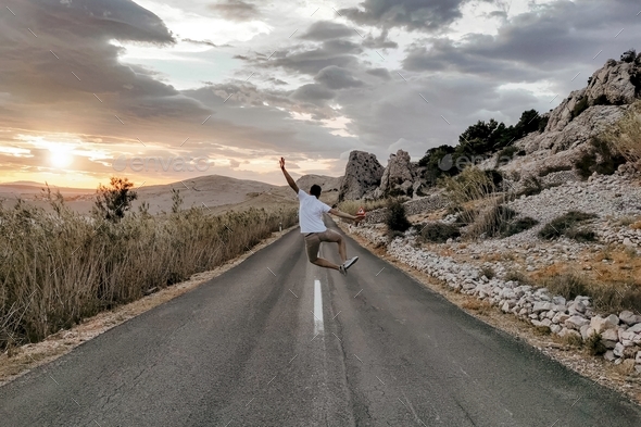 Young man in white t-shirt jumping in the middle of road, sunset, summer, happy, inspirational.