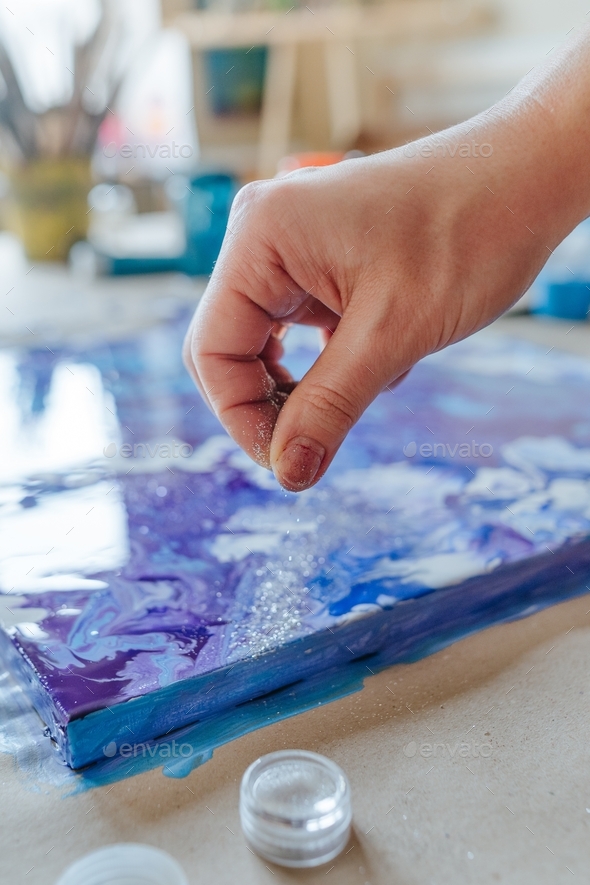 Female artist\'s hand sprinkling silver glitter on the fluid art picture.