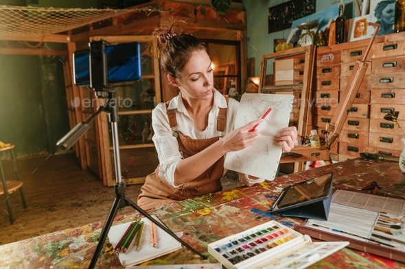Female artist blogger at art studio recording her drawing master class using smartphone. Online educ