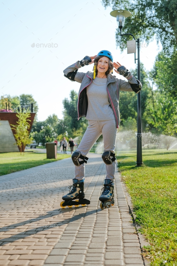 Happy mature woman rollerblading in the park wearing helmet, protective helmet, knee pads, elbow pad