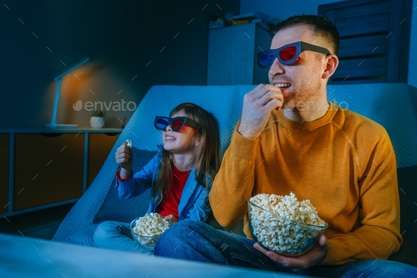 Father and daughter watching movie at home using 3D eye glasses