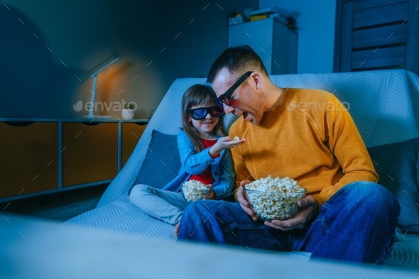Father and daughter watching movie at home using 3D eye glasses