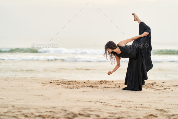 a dancer in a black dress on the beach expressing strength and courage in her movements