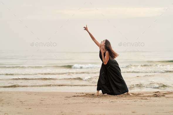 a dancer in a black dress on the beach expressing pain and passion in her performance