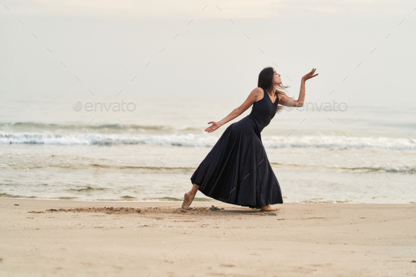 a dancer in a black dress on the beach expressing strength and courage in her movements