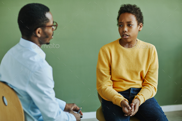 Upset schoolboy in casualwear describing his problem to psychologist