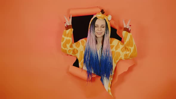 Young Woman in Pajamas of Giraffe Posing in Hole of Orange Background alt