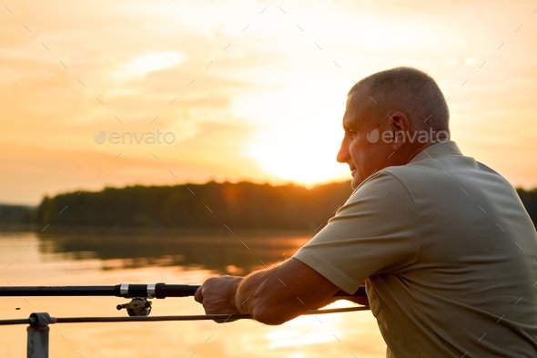 An adult man with a fishing rod on the shore of the lake is