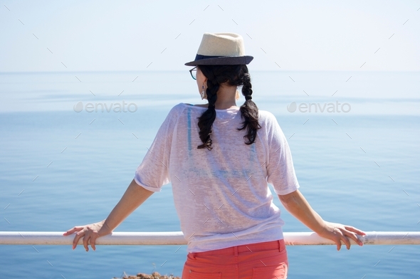 Close up portrait of woman from behind with a hat, looking into the sea leaning on a railing