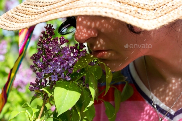 A young woman in a straw hat smells of lilac