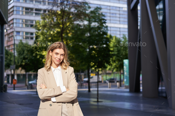 Portrait of smiling businesswoman in corporate clothing, looking confident and happy, wearing beige