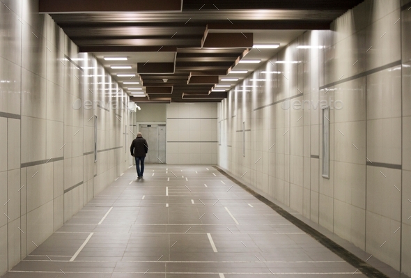 A man from behind walking alone in the subway corridor under electricity lights