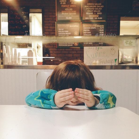 Child in fast food restaurant holding hands in front of face.