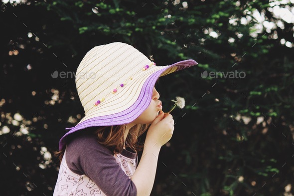 Girl in floppy hat blowing dandelions.