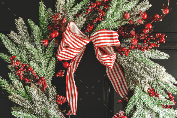 Christmas wreath decorated with red berries and a red and white striped bow on a black front door