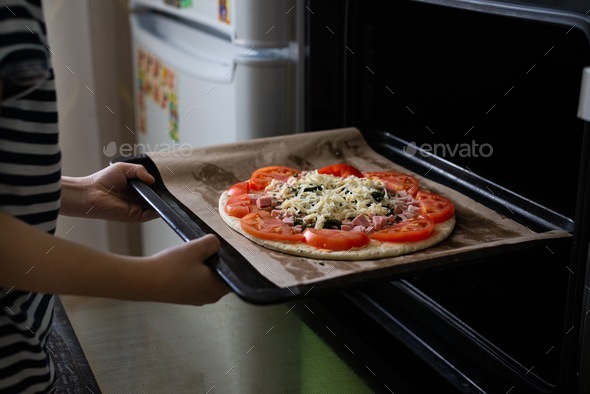 Home cooking, the child\'s hands hold a pizza pan in their hands, pizza baking in the oven