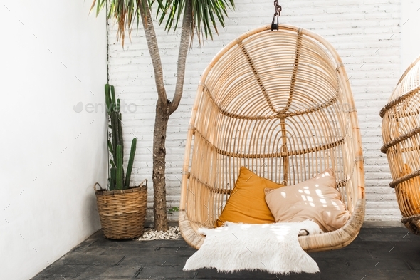 Wicker rattan hanging chair in loft cafe. Eco friendly furniture style and concept. Orange pillows