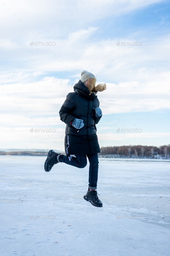 Happy teenage girl playing with snow and jumping on ice. Stock Photo by