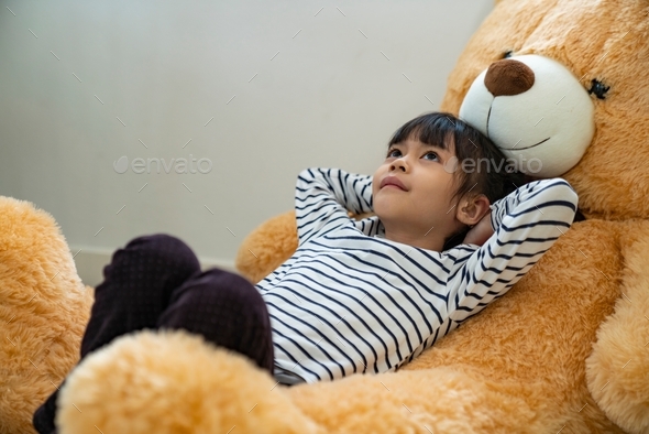 A girl with hearing loss wearing a hearing aid lies on top of a big bear.