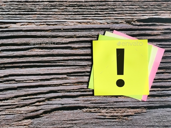 Colorful sticky note written exclamation mark isolated on wooden background.