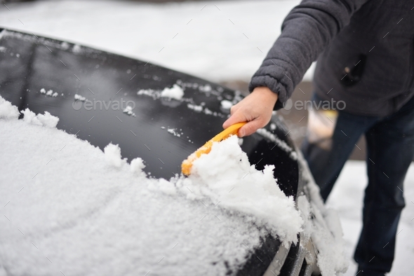 A human hand cleans the car from snow with a special brush. A hand sweeps snow from the hood of the