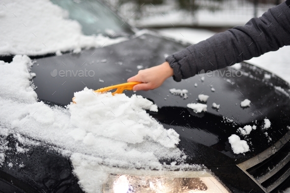 A human hand cleans the car from snow with a special brush. A hand sweeps snow from the hood of the