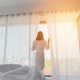Back view of female in bathrobe touching curtains and looking out window while standing in stylish - PhotoDune Item for Sale