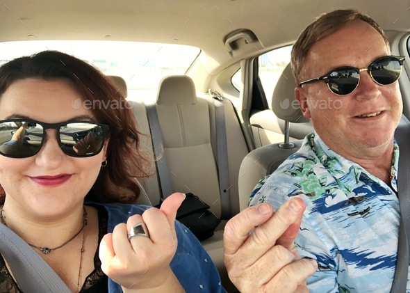 Father and daughter wearing sunglasses and snapping fingers sharing a cool time in car on road trip
