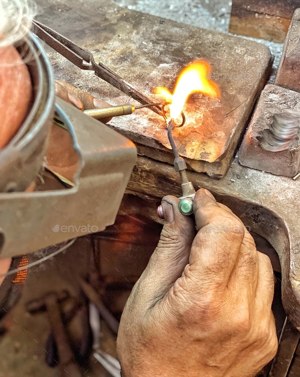 Goldsmith craftsman melts gold with hot torch as he repairs a ring in his shop with his rugged hands