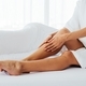 Caucasian female spreading smooth cream on soft legs skin while sitting on comfortable bed at home - PhotoDune Item for Sale