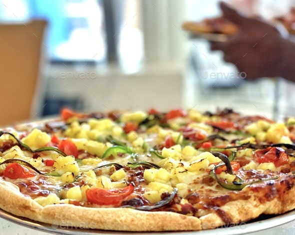 Pizza with colorful vegetarian toppings served at a local restaurant by a diverse server
