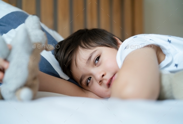 Happy boy waking up in the morning with big smile, Healthy child lying in bed playing with dog toy,