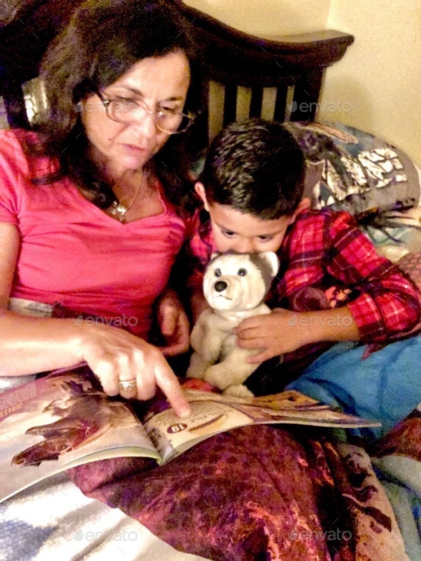Grandma reading a book to her grandson while in bed.