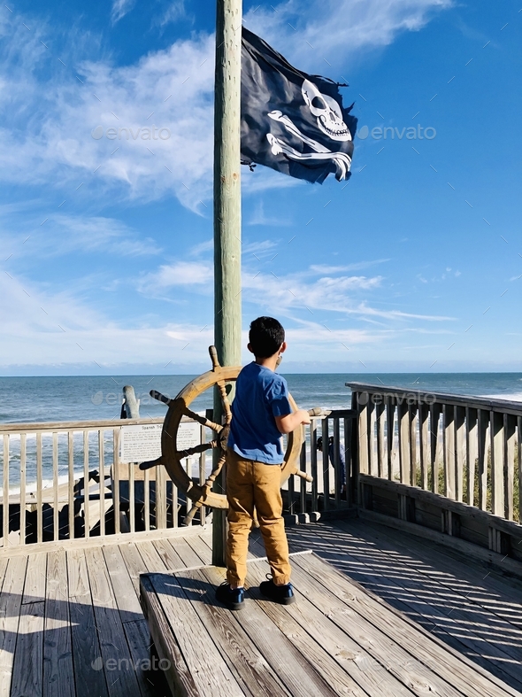 Small child playing captain of a ship on a makeshift pirate ship, with a pirate’s flag.