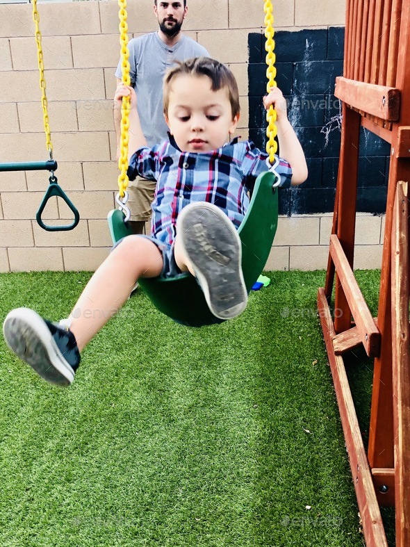 Dad pushing his son on the swing.