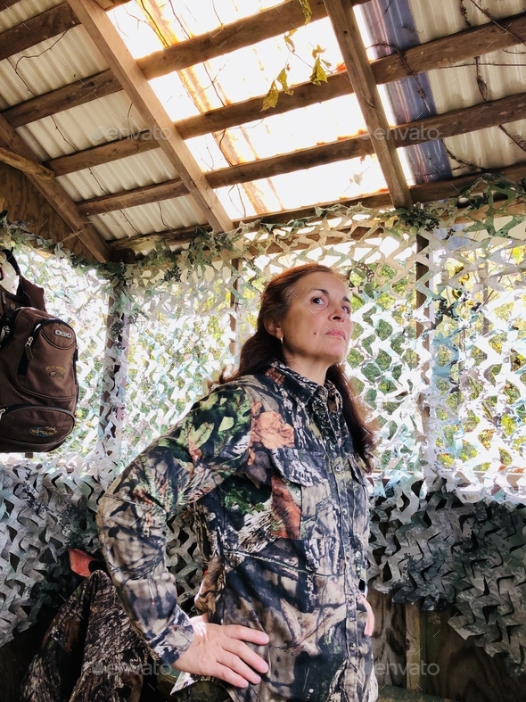 Woman wearing hunting clothes standing in her blind.