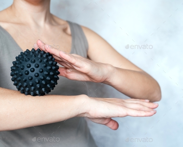A young woman massages her elbow with a spiky trigger point ball, tennis elbow exercises