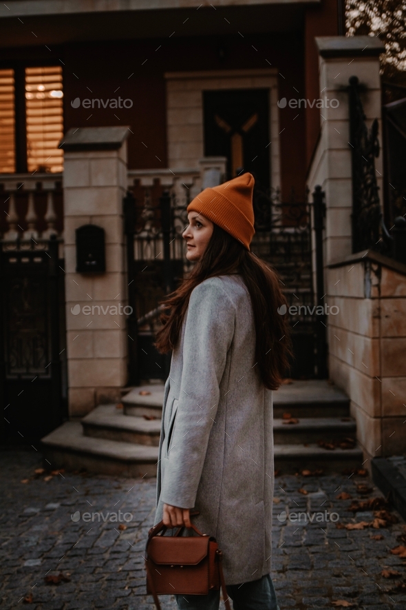 A woman is standing near a beautiful house on the street in the autumn season alone. Street outfit