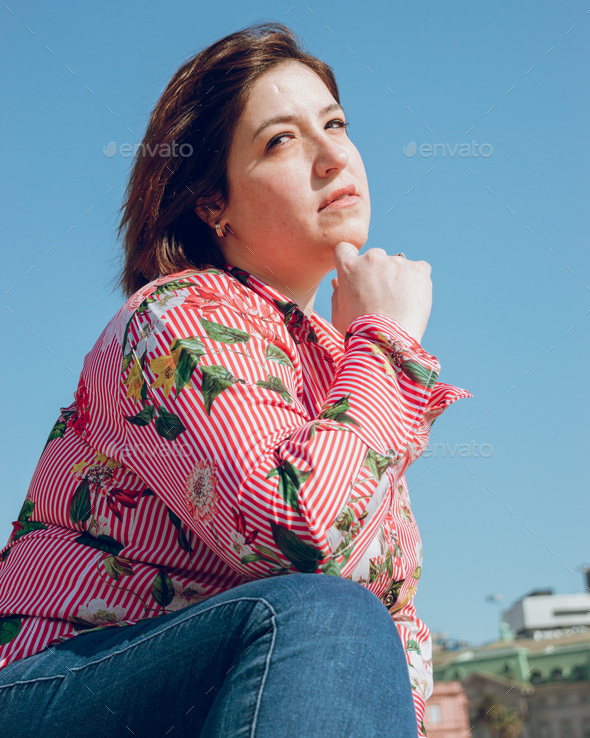 beautiful young woman posing crouched with a pensive face and a hand on her chin, vertical image