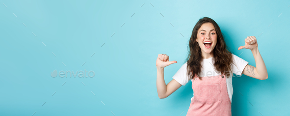 Pick me. Cheerful young girl pointing at herself and smiling, self-promoting, volunteering, looking