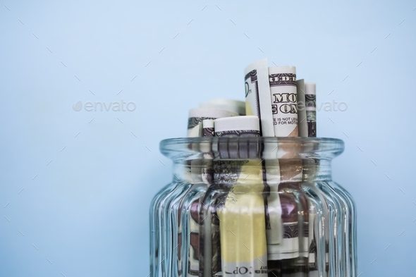 Cash money bank note 100 dollars in glass jar bottle with blue background.