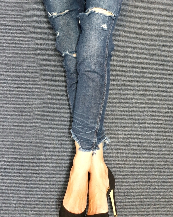 Lower section of woman wearing denim jeans with black shoes on grey carpet background