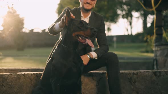 A Rich Businessman in a Business Suit Walks with a Big Doberman in the Park. A Successful Bearded alt