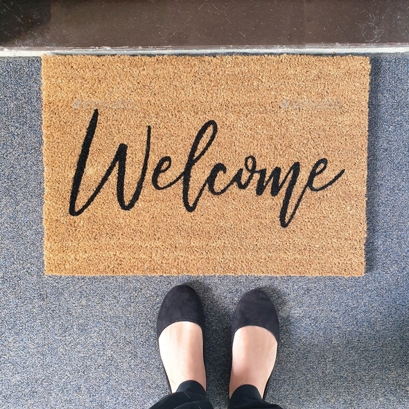 low section of woman standing under welcome mat in front of entrance