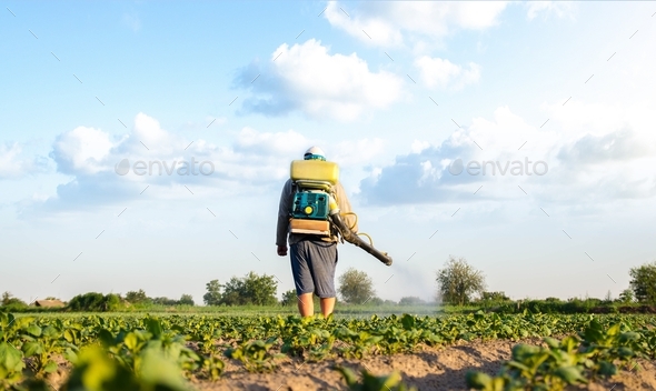 Farmer with a mist sprayer walks through farm field.