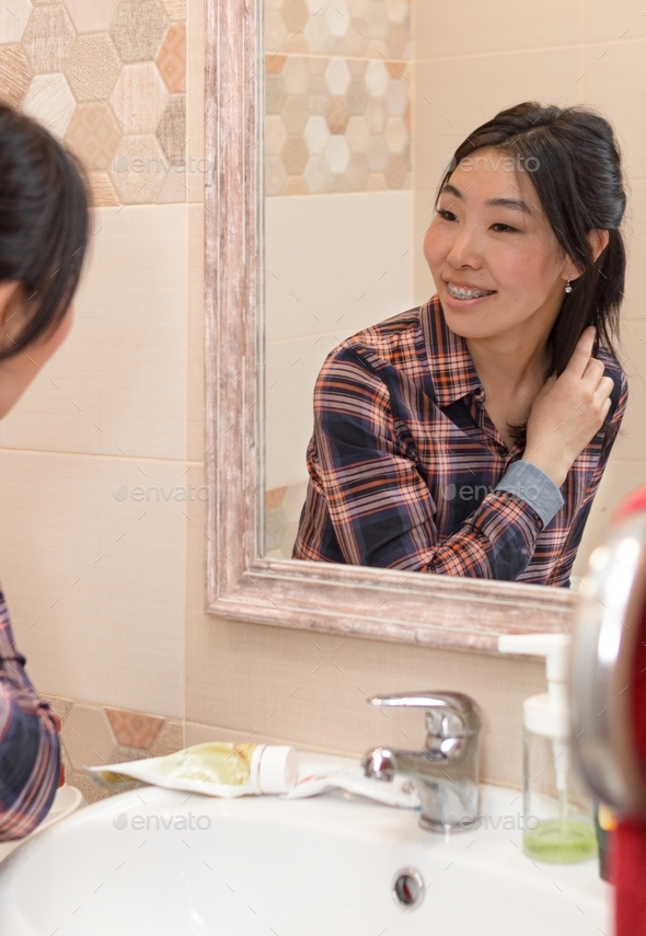 Reflection of happy woman with braces in bathroom mirror, healthy