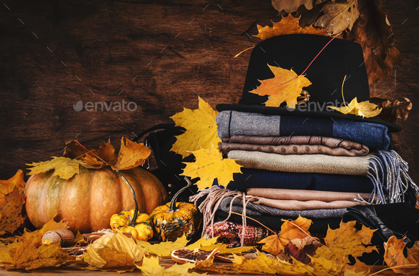 Autumn background with warm autumn and winter clothes, scarves, sweaters, felt hat, gloves, pumpkins