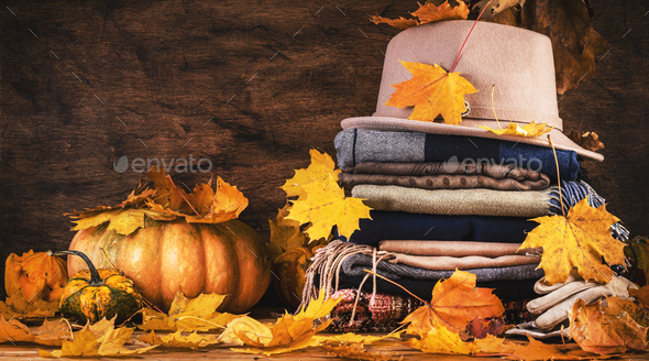 Autumn background with warm autumn and winter clothes, scarves, sweaters, felt hat, gloves, pumpkins