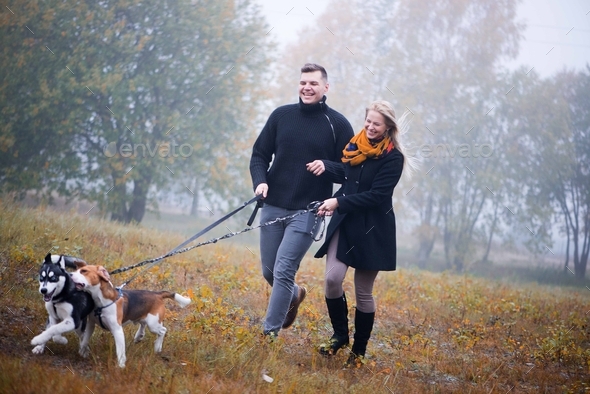 happy couple with two dogs running in misty autumn park