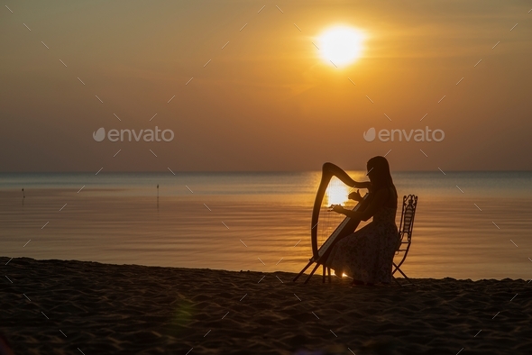 beautiful woman playing celtic harp at beach during sunset